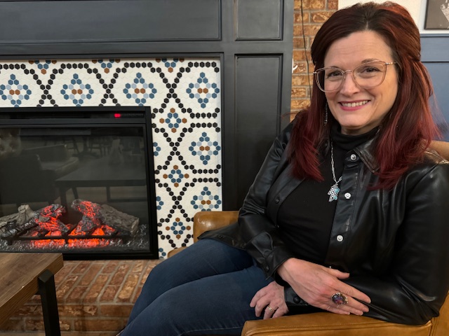 Michele Weisman sitting at a coffee shop and fire place in the back ground.